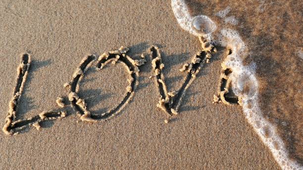 istock Love Word Written on Sandy Beach and Wiped Out by Sea Wave at Sunset 1298623322