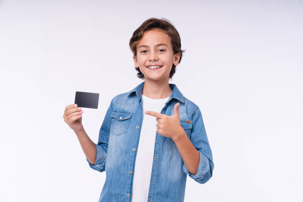 menino sorridente apontando para cartão de crédito em traje casual isolado sobre fundo branco - cartão de saudações - fotografias e filmes do acervo