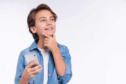 Close up portrait of small caucasian boy taking a thought with smart phone isolated over white background