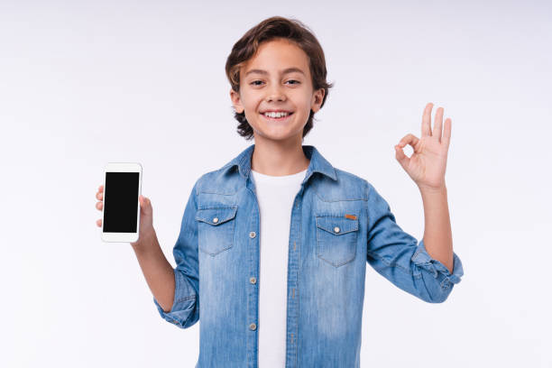 istock Young caucasian boy showing okay gesture with phone isolated over white background 1298623343