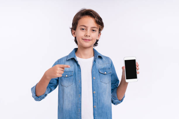 istock 10s caucasian boy pointing at smart phone isolated over white background 1298623355