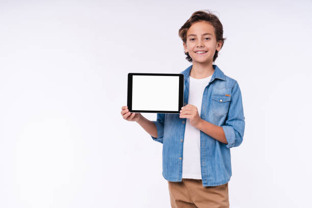 улыбающийся маленький мальчик в повседневной одежде, представляя пустой экран планшета, изолированный на белом фоне - ipad mini ipad white small стоковые фото и изображения