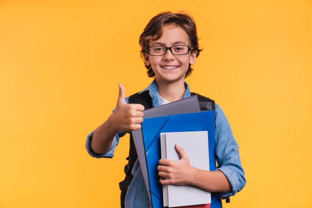 黄色の背景の上に隔離された学校でスタッドのための本とメガネとカジュアルな服装でインテリジェントな10年代の白人の少年 - thumbs up book smiling student ストックフォトと画像
