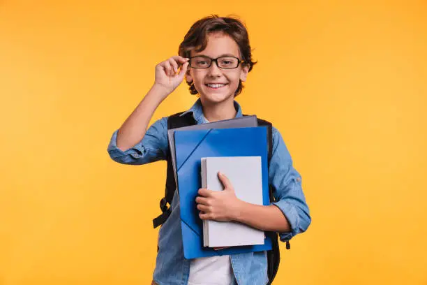 Photo of Clever young boy holding folders for studing at school isolated over yellow background