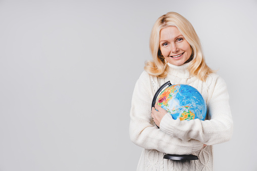 Middle-aged caucasian woman in casual clothing holding the globe isolated over grey background. Save the planet concept