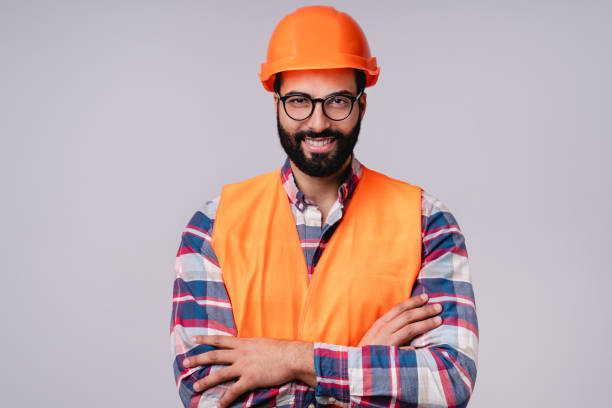 istock Confident handsome Arabic construction worker in special uniform and hardhat with arms crossed isolated over grey background 1298633532