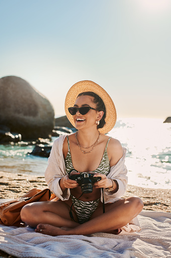 Shot of a young woman holding a camera while spending time at the beach