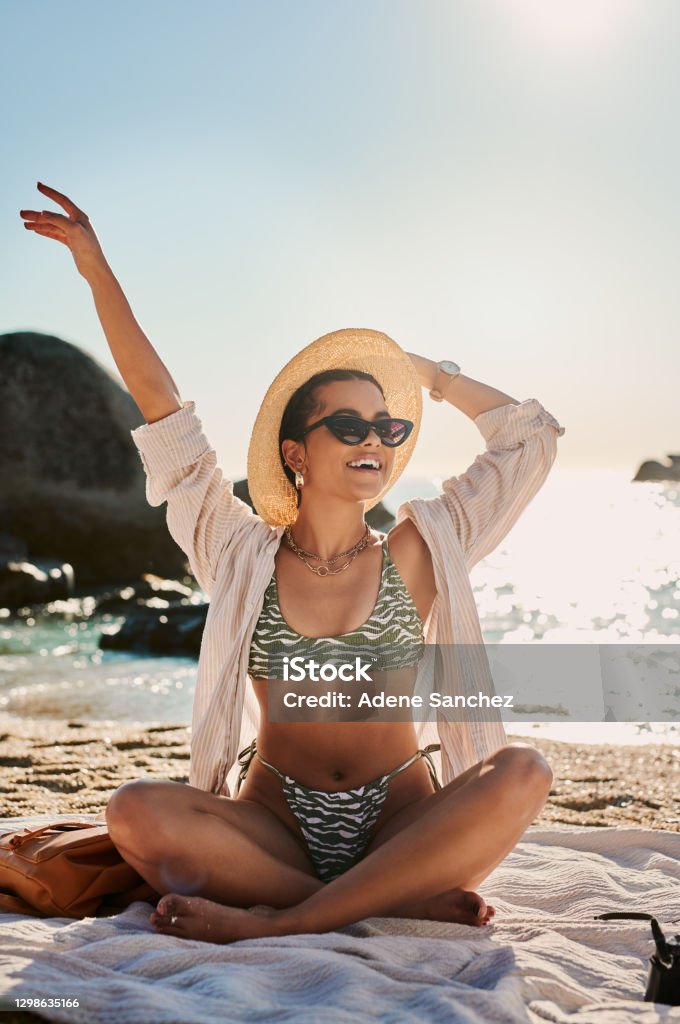 I’m nicer when I’m at the beach Shot of a beautiful young woman sitting on the beach Sunglasses Stock Photo