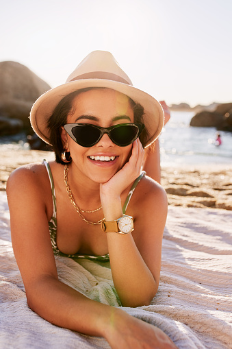 Shot of a woman wearing sunglasses while lying on the beach