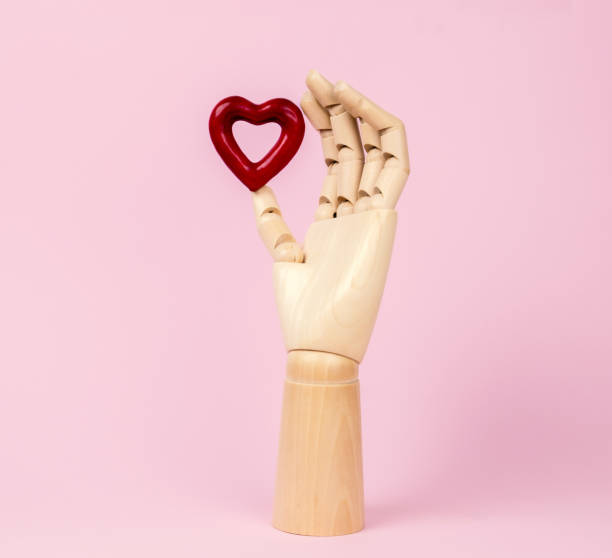 istock Human wooden hand model with heart on pastel pink. 1298638385