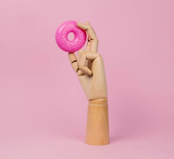 Wooden hand with pink donut on a pastel pink background.
