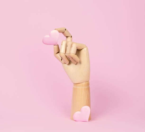 Human wooden hand model with heart on pastel pink.