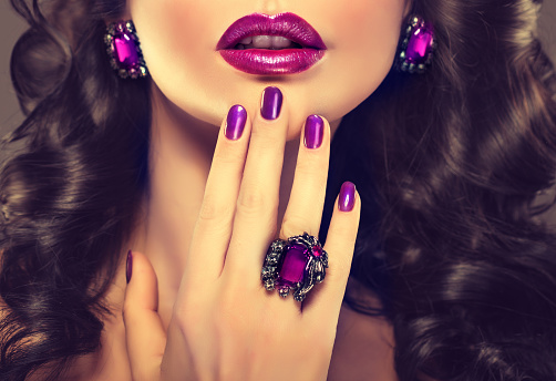 Splendid evening makeup and jewellery in a purple tints.Graceful fingers, decorated by big ring and accurate violet manicure, in front of the well shapep lips colored in purple. evening makeup and manicure.