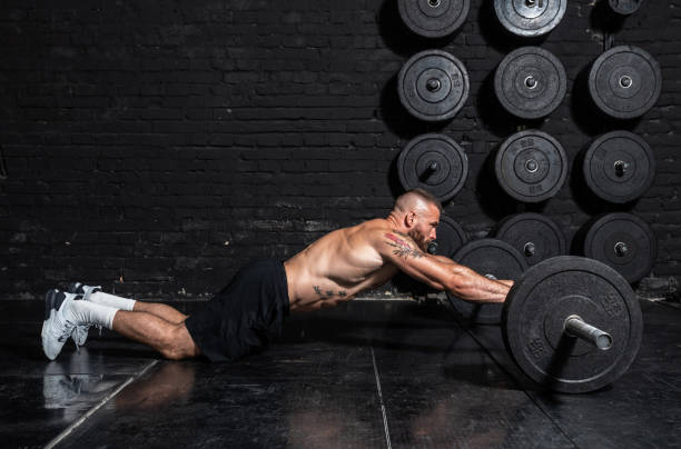 istock Young active strong fit sweaty muscular man with big muscles doing abs workout by rolling barbell weights in the floor of the gym as hardcore cross training real people exercise 1298645892
