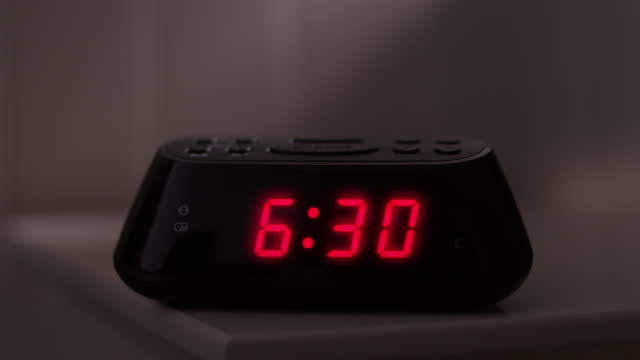 Digital alarm clock, time from 6.29 to 6.30. Glowing numbers.