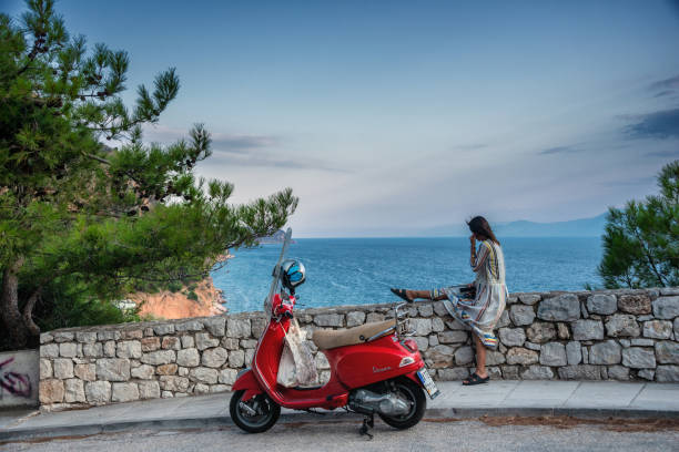 young woman with red motor scooter sitting on wall high above naflio, greece - vespa scooter imagens e fotografias de stock
