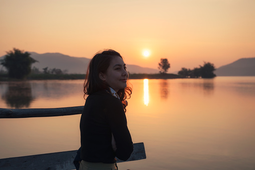 Beautiful young asian woman enjoying with sunrise on mountain lake at the morning