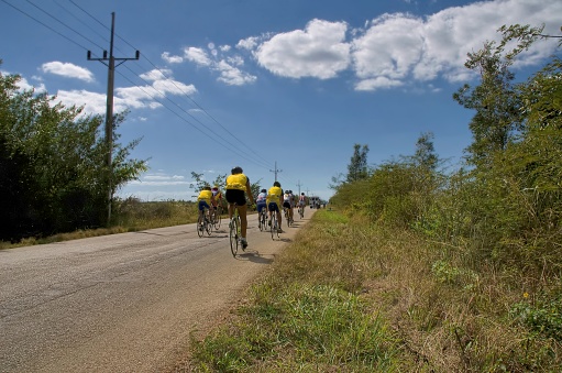 Matanzas, Cuba - January 29,2008 : A large peloton, eight men, rides down Cuban Route 11 at noon on a bright winter day against a background of a rich blue sky and cumulus clouds with tour bus of birdwatchers ahead of them near the Caves of the Fish on the bay of Pigs