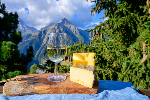 Glass of swiss or savoy dry white wine, tomme and emmental cheese with Alpine mountains peaks on background in sunny day