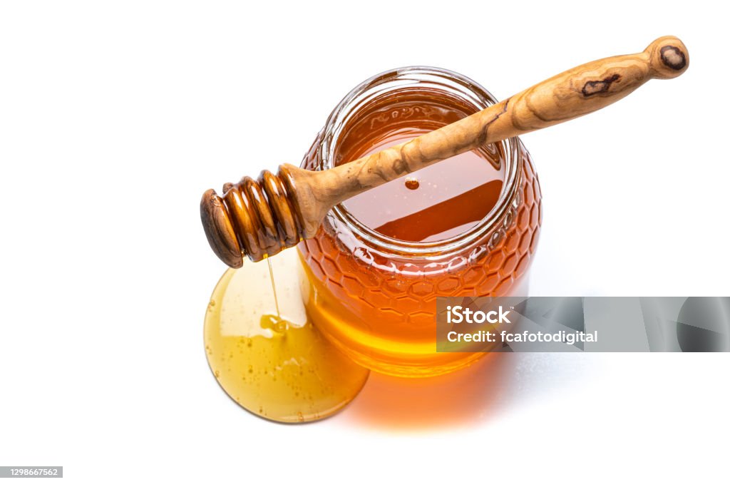 Honey jar and honey dipper shot from above on white background. Copy space Overhead view of an open honey jar wit a wooden honey dipper on it isolated on white background. Predominant colors are gold and white. The composition is at the right of an horizontal frame leaving useful copy space for text and/or logo at the left. High resolution 42Mp studio digital capture taken with Sony A7rII and Sony FE 90mm f2.8 macro G OSS lens Honey Stock Photo