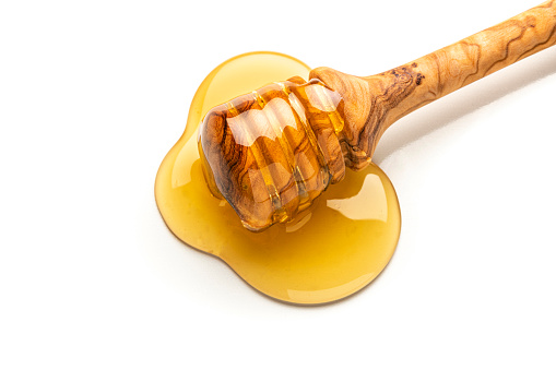 Close up view of a honey dipper with dripping honey isolated on white background. Predominant colors are gold and white. The composition is at the right of an horizontal frame leaving useful copy space for text and/or logo at the left. High resolution 42Mp studio digital capture taken with Sony A7rII and Sony FE 90mm f2.8 macro G OSS lens
