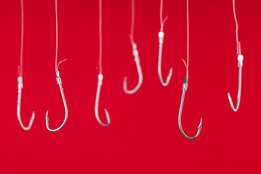 Fishing hooks are hanging with transparent string in front of red background.