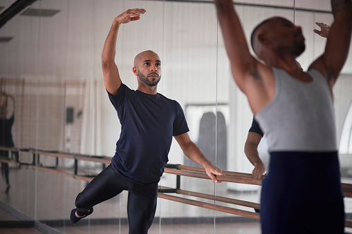 Two african-american male dancers practising ballet on barre in dance studio