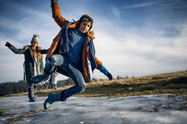 Kids playing and sliding on patch of ice on hill meadow