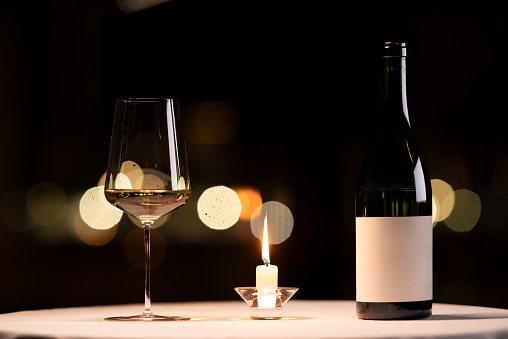 Glass of white wine and wine bottle on a restaurant table.