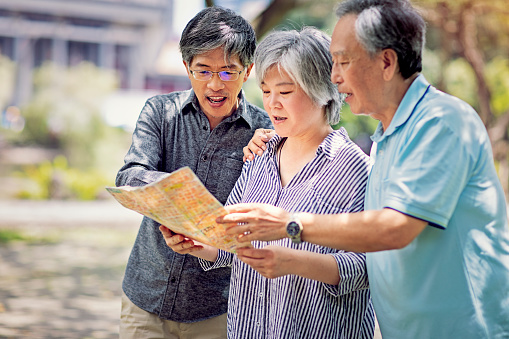Asian mature friends are looking in a map for direction on the street