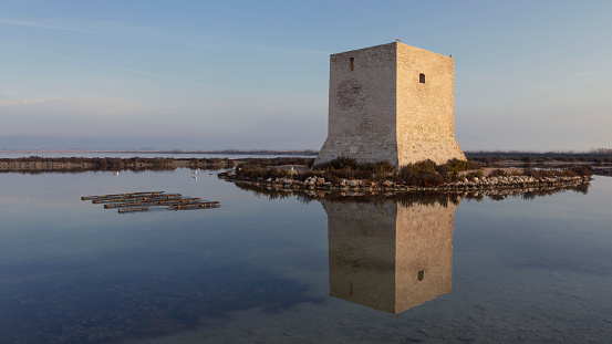 Sunrise in a sea salt flat in which an old stone watchtower stands out in Santa Pola (Alicante, Spain). Some seagulls appear perched on the surface.