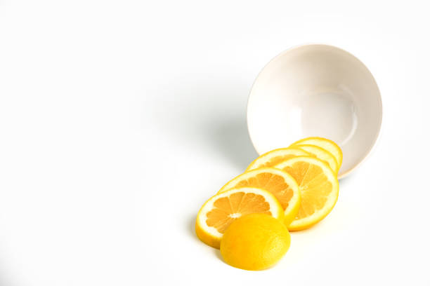 Four vibrant yellow lemons arranged on a clean white surface, illuminated to emphasize their texture and bright color.