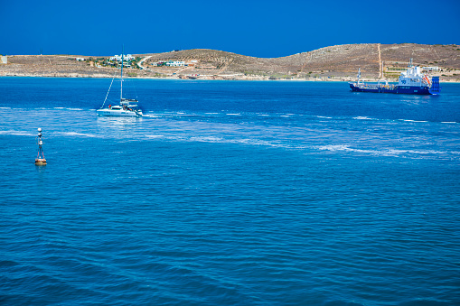 Paros island, Greece - July 03, 2018: View of part of Paros island in the Agean Sea, Greece. You can see a small boat and tanker ship anchored in front of the island.