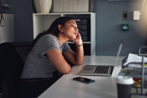 Her motivation is dwindling Shot of a young businesswoman looking bored while working on a laptop in an office at night wasting time photos stock pictures, royalty-free photos & images
