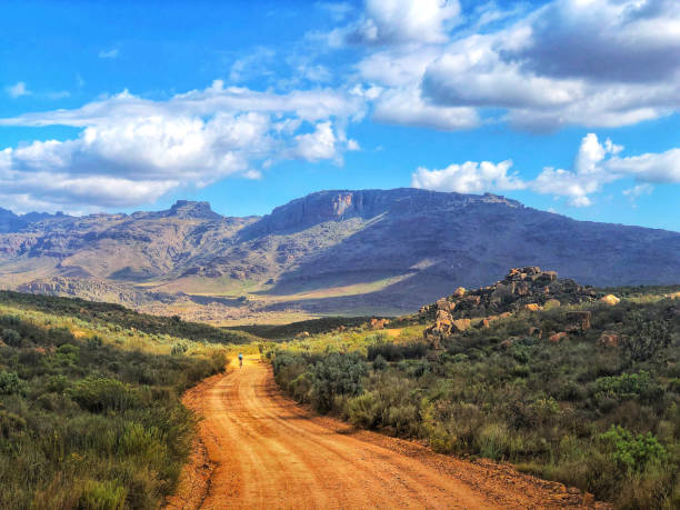 Picturesque Cycling Mountain biking downhill on gravel road towards the mountains with clouds freedom Picturesque Cycling Mountain biking downhill on gravel road towards the mountains with clouds freedom Kromrivier Sanddrif Dwarsrivier Matjiesvlei Cederberg Wilderness Western Cape South Africa fynbos photos stock pictures, royalty-free photos & images