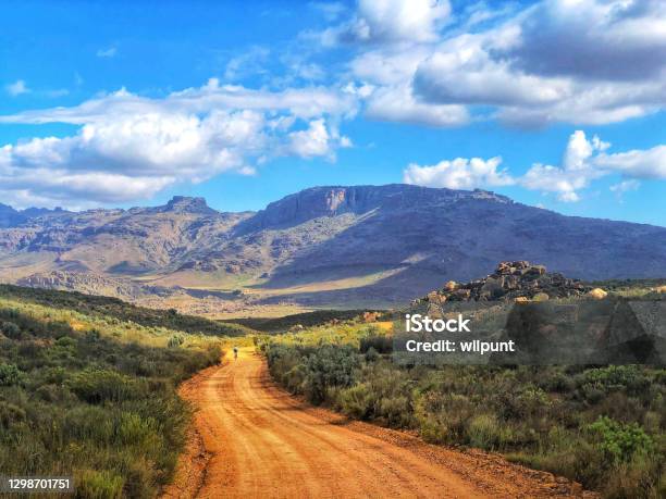 Picturesque Cycling Mountain Biking Downhill On Gravel Road Towards The Mountains With Clouds Freedom Stock Photo - Download Image Now
