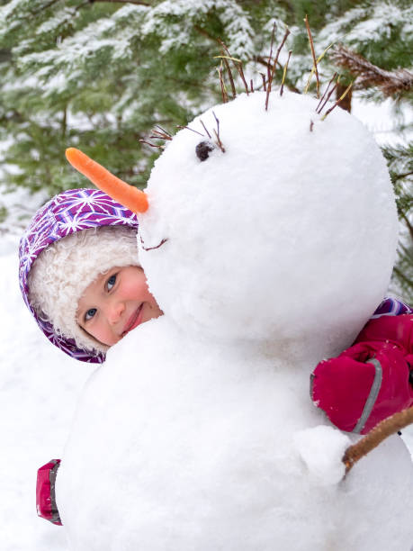 ein kind, ein 5 jahre altes kaukasisches mädchen, hat einen schneemann geblendet und umarmt ihn und lächelt. alle arten von spaß im freien im winter. - child winter snow 4 5 years stock-fotos und bilder
