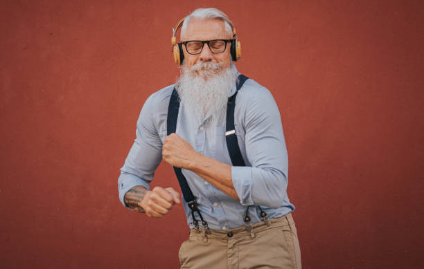 an older man in hipster clothes and glasses and long white beard listens to music and dance happily in the street focus on head stock photo