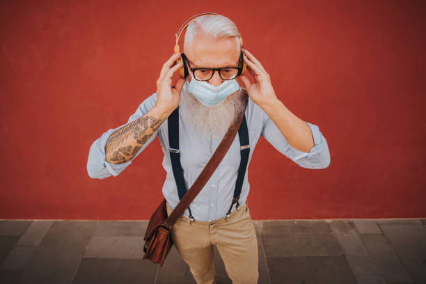 an older man in hipster clothes and glasses and long white beard listens to music and dance happily in the street focus on head stock photo