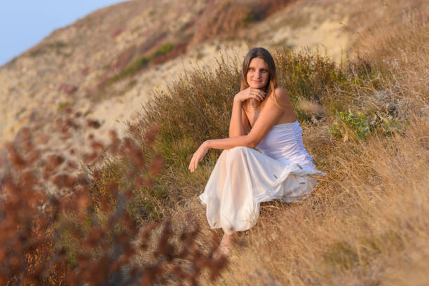 istock Beautiful girl sitting on a hillside at sunset 1298709967