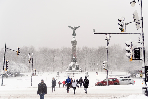 Unidentified people crossing street in front of the angel of Mount-Royal during snow storm. This was taken in Jeanne Mance park in front of Mount Royal. Horizontal outdoors full length shot with copy space.