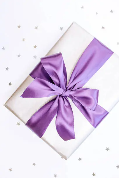 Beautiful box-gift in silver paper with trendy violet ribbon and bow-knot and sprickle stars. Holiday concept. Top view.