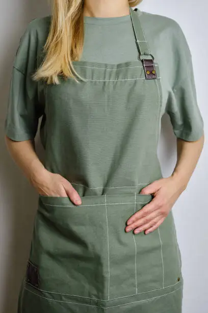 A woman in a kitchen apron. Chef work in the cuisine. Cook in uniform, protection apparel. Job in food service. Professional culinary. Green fabric apron, casual clothing. Handsome baker posing