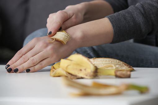 Woman rubbing banana peel on her hands to hydrate skin. Zero waste and natural skin care concept.