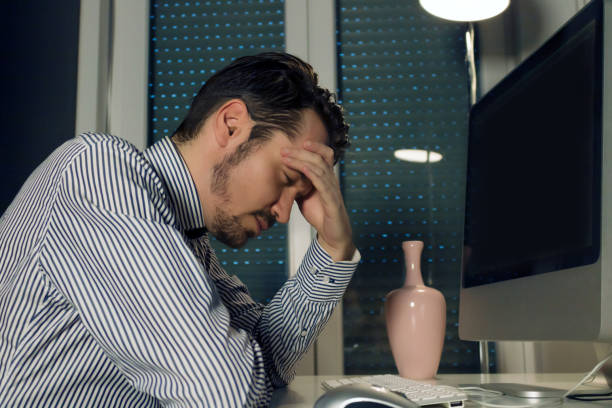 istock Male entrepreneur holding his head in pain while working late on a computer. 1298739348