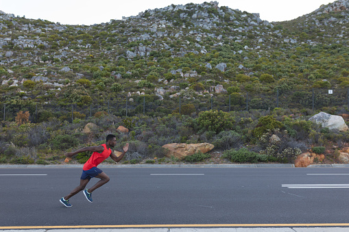 Fit african american man in sportswear running on a coastal road. healthy lifestyle, exercising in nature.