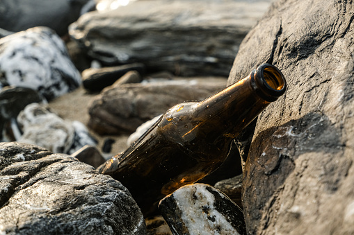 Empty glass beer bottle on rocky sea shore,polluted coast in cilento,italy.