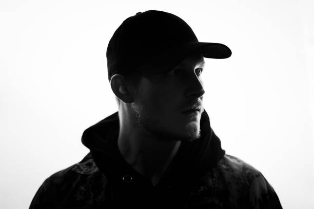 Young Man Bright Backlit Silhouette Urban Portrait Young man with baseball cap looking over to his friends. Bright Backlit Silhouette Portrait. Millennial Generation Real People Urban Street Portrait. back lit stock pictures, royalty-free photos & images