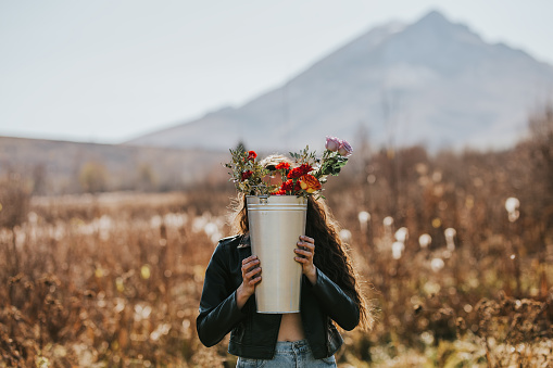 Woman holding a tall iron bucket with flowers in the open air in nature.