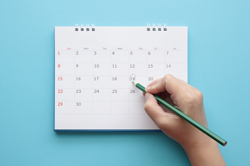 Hand with pencil mark on calendar date on blue background
